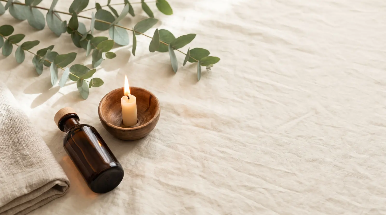 Styled flat lay of linen, eucalyptus and a lit candle, representing a calm home treatment setting